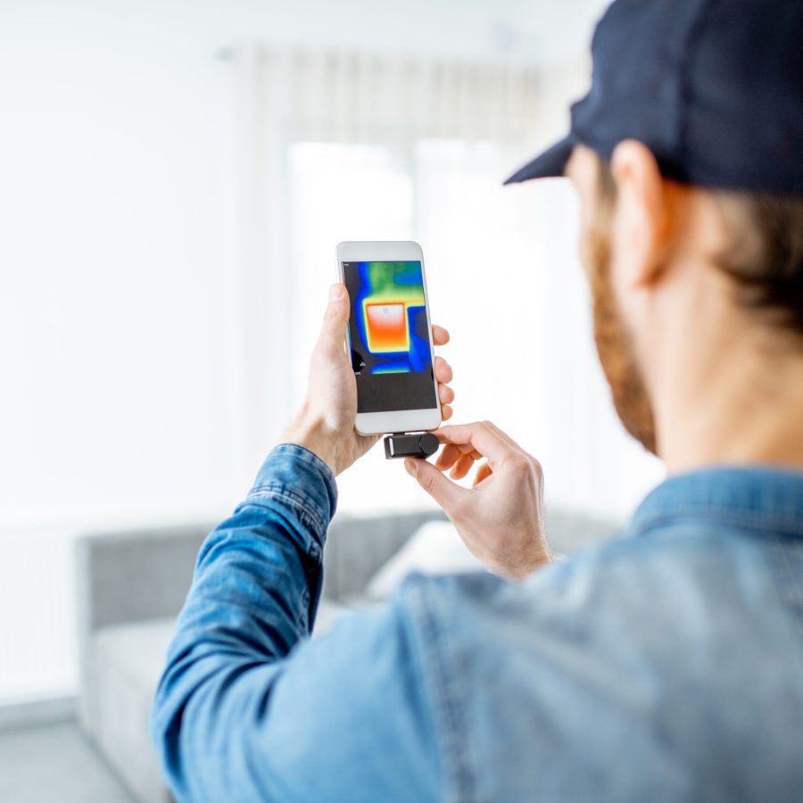 Man checking the house heat loss and the temperature of radiator with thermovision camera and smart phone in the house